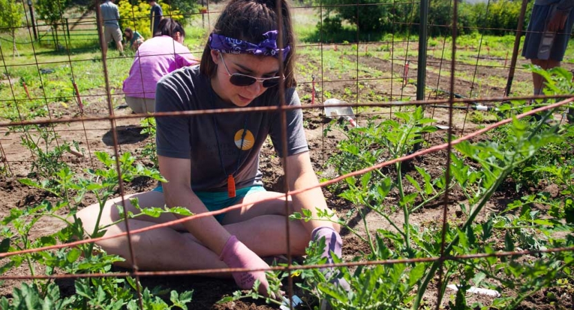 a student wearing gloves sits and works in a garden during a service project with outward bound